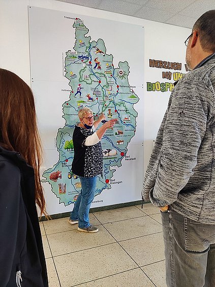 Eine Frau steht vor der Gebietskarte der Hessischen Rhön und eräutert diese den Zuhörern.