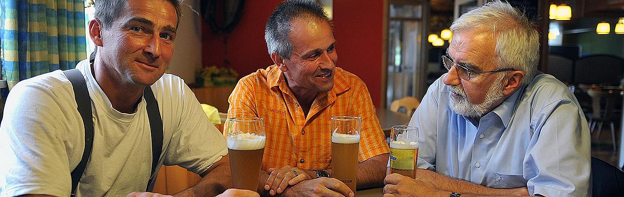 Drei Männer sitzen an einem Tisch und unterhalten sich. Sie trinken dazu Bier.